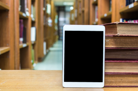 Tablet computer with old books on the wood table in library, Education conceptの写真素材