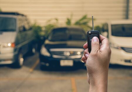 Hand holding and touching the keys over photo blurred of used car for open the door car, transportation and ownership conceptの写真素材
