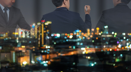 double exposure of Businessman group standing and working in night office over the cityscape phoro blurred background, business hard working conceptの写真素材