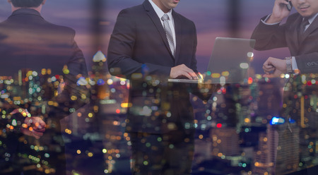 double exposure of Businessman group standing and working in night office over the cityscape phoro blurred background, business hard working conceptの写真素材