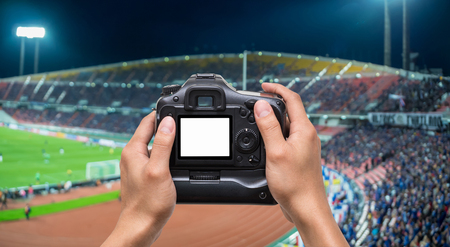 Hand holding the camera over Abstract blurred photo crowd of spectators on a stadium with a football match, sport background conceptの写真素材