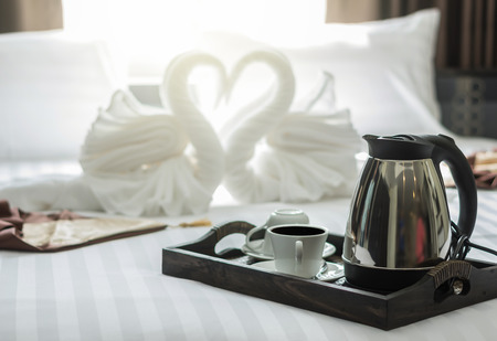 elegant coffee cup set on wooden trey in modern bedroom interior with blurred background of two nice towels swans with pillowの写真素材