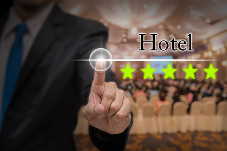 Businessman pointing five star button to increase rating of hotel over Abstract blurred photo of conference hall or seminar room with attendee background, business evaluation concept, Increase ratingの写真素材