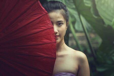Closeup Portrait of beautiful Village women standing with red color traditional umbrell in forest, countryside and Folkways conceptの写真素材