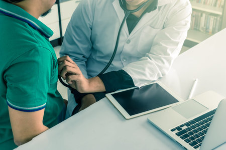 Doctor is consulting with Patient about his health on working desk which using technology tablet at...
