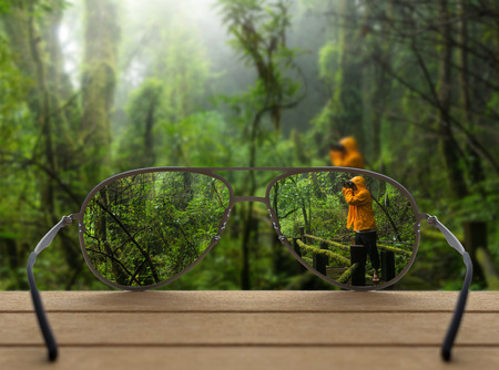 Conceptual image of rain forest focused in glasses lenses over the photo blurred of Traveller taking photo at Beautiful rain forestの写真素材