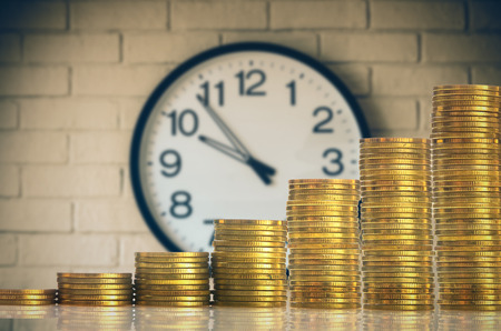 stacks of gold coins step over the vintage clock on the wall background, investment and financial conceptの写真素材