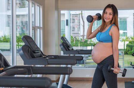 Portrait of asian Pregnant female do exercise in sports room, lifting dumbbells, healthy motherhood conceptの写真素材