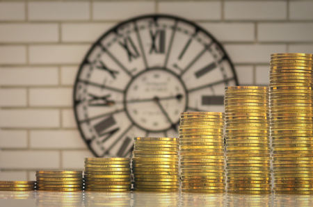 stacks of gold coins step over the vintage clock on the wall background, investment and financial conceptの写真素材
