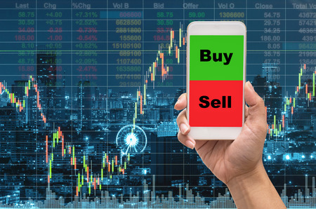 Female hand holding mobile phone touch screen showing buy and sell over the Stock market exchange information and Trading graph on the cityscape at night background,Business trading concept Female hand holding mobile phone touch screen showing buy and sell over the Stock market exchange information and Trading graph on the cityscape at night background,Business trading concept