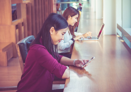 Asian Businesswomen using the smart phone over the blurred photo of coworker background In the modern creative Office, business technology conceptの写真素材
