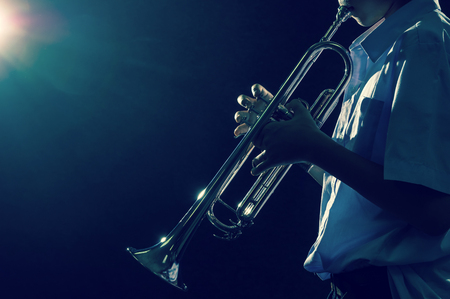 Young student Musician playing the Trumpet with spot light and len flare over dark background on the stage, Musical conceptの写真素材