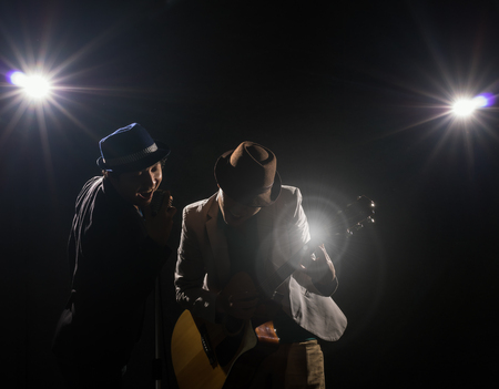 Musician Duo band hand holding the microphone and singing a song and playing the guitar on black background with spot light and lens flare, musical conceptの写真素材