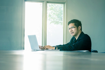 Happy asian businessman sitting on working space and using laptop in the modern Office or coffee shop. business technology conceptの写真素材