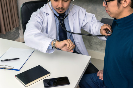 Doctor using stethoscope for checking heart rate and consulting with Patient about his health on working desk at hospital, physician conceptの写真素材