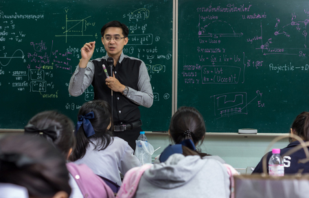 Asian teacher Giving Lesson to group of College Students which answer the question in the classroom over the physics formular in thai laguage on black board, school education conceptのeditorial素材