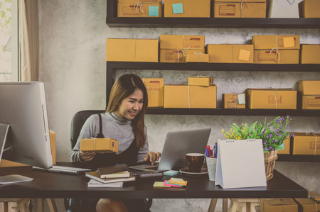 Young asian teenager owner business woman work at home for online shopping, checking order and prepaing package the product with office equipment, entrepreneur and alpha generation life style conceptの写真素材