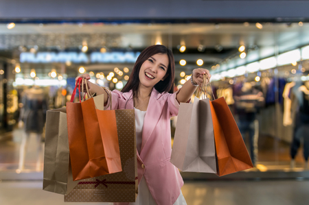 Happy young asian woman shopping in happy feeling and holding the product paper bag over the Abstract blurred photo of clothing store in a shopping mall, shopping conceptの写真素材