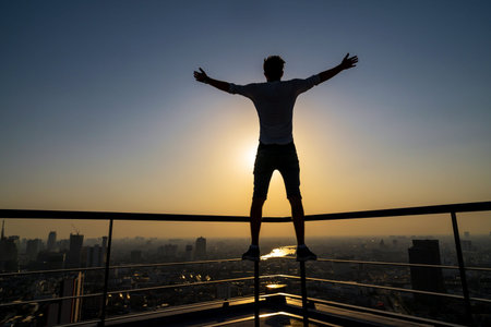 Silhouette of man standing with extend arms action over the cityscape background at sunset time with...