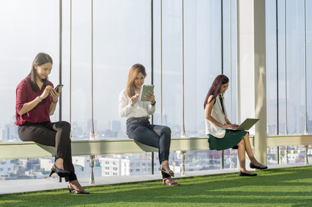 Three women using social network each technology equipment In the modern creative Office beside the windows at the evening, business social network conceptの写真素材
