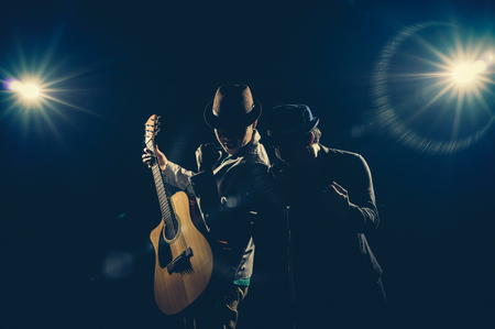 Musician Duo band hand holding the microphone and singing a song and playing the guitar on black background with spot light and lens flare, musical conceptの写真素材