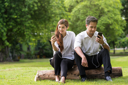 Happy asian couple using and listening the song via smart phone camera in the park, lover and lifestyle conceptの写真素材