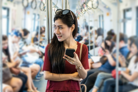 Asian woman passenger with casual suit using the social network via smart mobile phone in the BTS Skytrain rails or MRT subway for travel in the big city, lifestyle and transportation conceptの写真素材