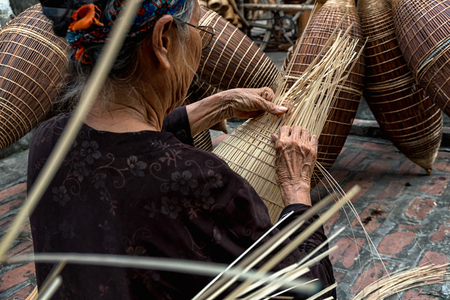 Closeup Old Vietnamese female craftsman hands making the traditional bamboo fish trap or weave at the old traditional house in Thu sy trade village, Hung Yen, Vietnam, traditional artist conceptのeditorial素材