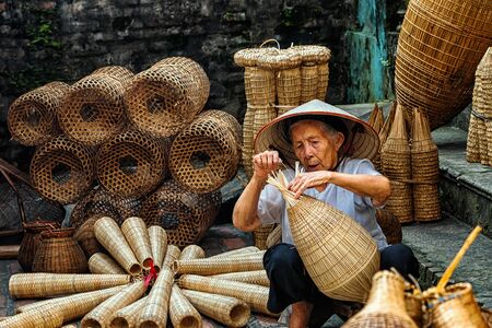 Old Vietnamese female craftsman making the traditional bamboo fish trap or weave at the old traditional house in Thu sy trade village, Hung Yen, Vietnam, traditional artist conceptの写真素材
