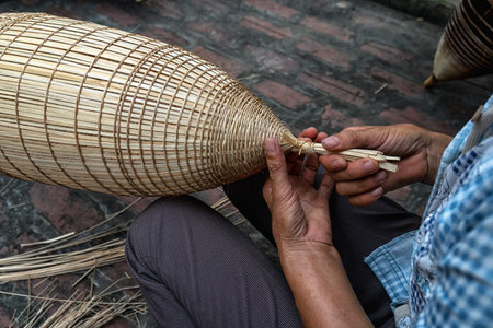 Closeup Old Vietnamese female craftsman hands making the traditional bamboo fish trap or weave at the old traditional house in Thu sy trade village, Hung Yen, Vietnam, traditional artist conceptの写真素材
