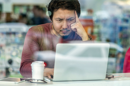 Portrait of asian businessman in casual suit using technology laptop for working in serious and exhausted action at the desk beside the glass in modern office,Business and lifestyle conceptの写真素材