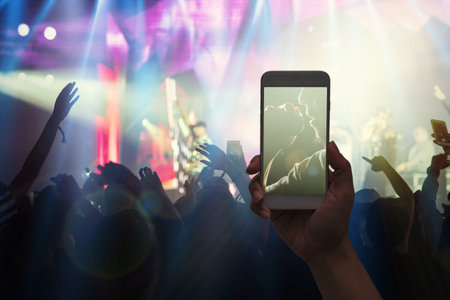Female hand holding mobile smart phone taking video record or Live stream of Concert crowd with...