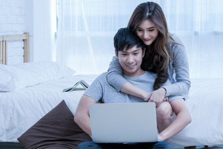 Closeup Happy Asian Lover or couple talking and smiling when using technology laptop on the bed in bed room at modern home, young women pointing to the nose of boyfriend, Lover and life style concept,の写真素材