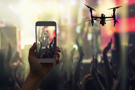 Female hand holding mobile smart phone and Drone flying taking video record or Live stream of Concert crowd and Music fanclub with show hand action, musical and concert conceptの写真素材