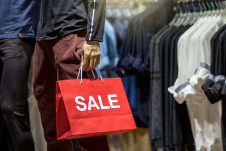 Part of male mannequin dressed in casual clothes holding the Sales paper shopping bag in the...