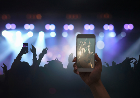 Female hand holding mobile smart phone taking video record or Live stream of Concert crowd with super star songer and silhouettes of Music fanclub with show hand action, musical and concert conceptの写真素材