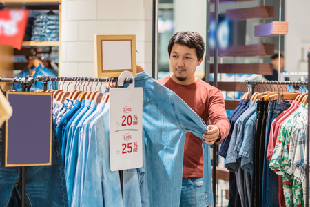 Smart asian man with beard choosing clothes in clothing store at shopping center, looking white jeans shirts , Fashion and Consumerism Concept.の写真素材