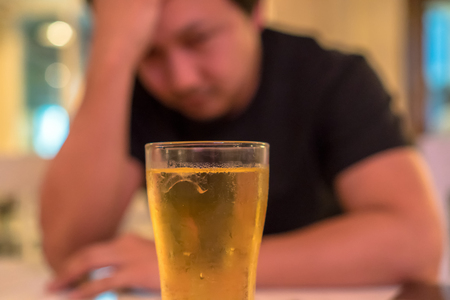 Asian young man in lonely and depressed action and holding head in hands and see glass of beer in pub and restaurant with low light place, depression and drinking conceptの写真素材