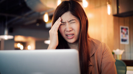 Asian businesswoman in casual suit working with computer in stress emotion at co-working space, business in depress and stressed conceptの写真素材