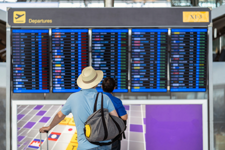 Back side of traveler with luggage standing over the flight board for check-in at the flight information screen in modern an airport, travel and transportation with technology concept.の写真素材
