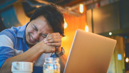 Asian businessman in casual suit working with computer in stress emotion at co-working space, business in depress and stressed conceptの写真素材