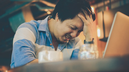 Asian businessman in casual suit working head in hand action with stress emotion at co-working space, business in depress and stressed conceptの写真素材