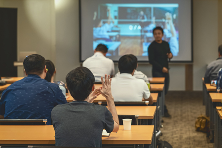 Speaker on the stage in front of the room with Rear view of Audience in put hand up acton for answer the question in the meeting or seminar meeting, business and education conceptの写真素材