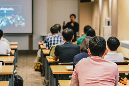 Speaker on the stage in front of the room with Rear view of Audience in put hand up acton for answer the question in the meeting or seminar meeting, business and education conceptの写真素材