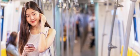 Banner, web page or cover template of Young Asian woman passenger using and listening music via smart mobile phone in subway train station, japanese,chinese,Korean lifestyle, leisure and daily life,の写真素材