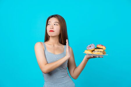 Attractive Asian young woman doing no action with donuts on isolated blue color background, weight loss and avoid junk food for dieting and Healthy concept, copy space and studioの写真素材