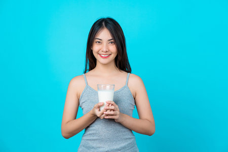 Attractive Asian young woman holding milk on isolated blue color background, weight loss and avoid junk food for dieting and Healthyの写真素材