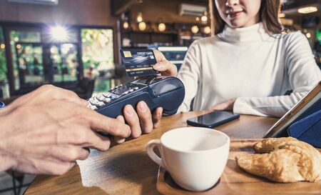 Closeup Asian customer woman paying with credit card via contactless technology to Asian Small Coffee shop owner at the female table in cafe,Small business owner and startup in coffee shop conceptの写真素材