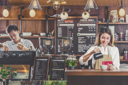 Asian Barista preparing cup of coffee, espresso with latte or cappuccino for customer order in coffee shop,bartender pouring milk,Small business owner and startup in coffee shop and restaurant conceptの写真素材
