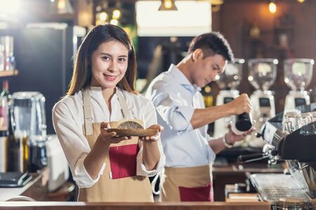 Asian Barista serving bakery cake, preparing cup of coffee, espresso with latte or cappuccino for customer order in coffee shop,Small business owner and startup in coffee shop and restaurant conceptの写真素材
